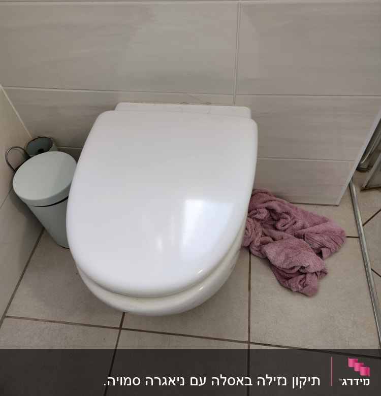 אסלה לבנה עם מגבת ורודה על הרצפה